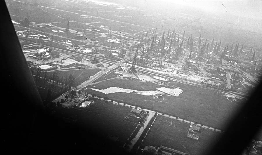 An aerial view of a massive, densely packed oil field filled with dozens of tall wooden oil derricks.