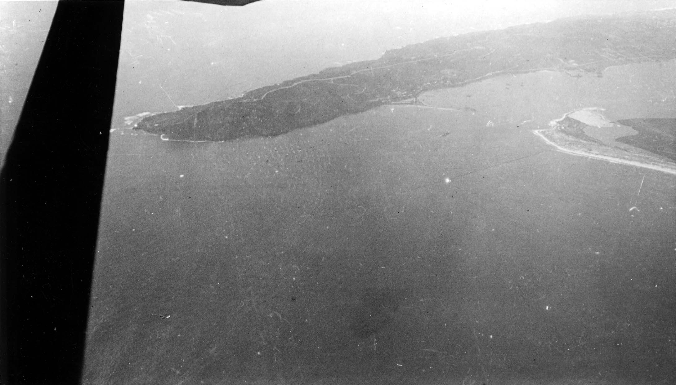 An authentic aerial photograph from an aircraft showing a wing strut and the Point Loma peninsula extending into the Pacific Ocean at the entrance to San Diego Bay.