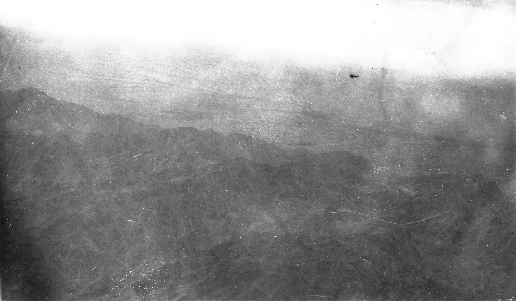 An aerial view of rugged, hazy mountain terrain captured from a high altitude.