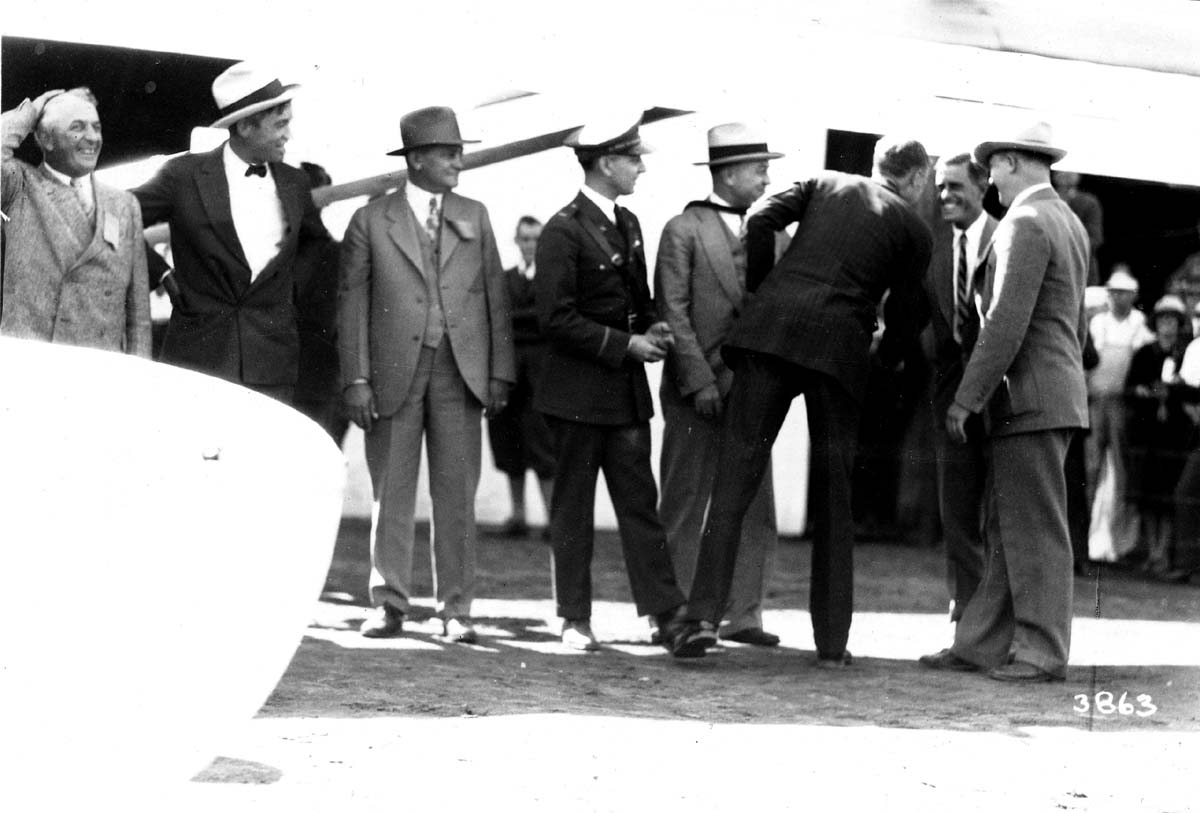 Archival photograph plate 3863 showing Charles Lindbergh greeting naval officers and civic leaders beneath an airplane wing.