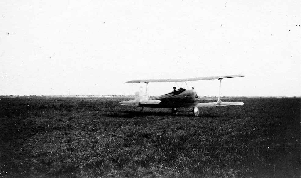 A single-engine biplane parked quietly in the middle of a vast, open grassy field.