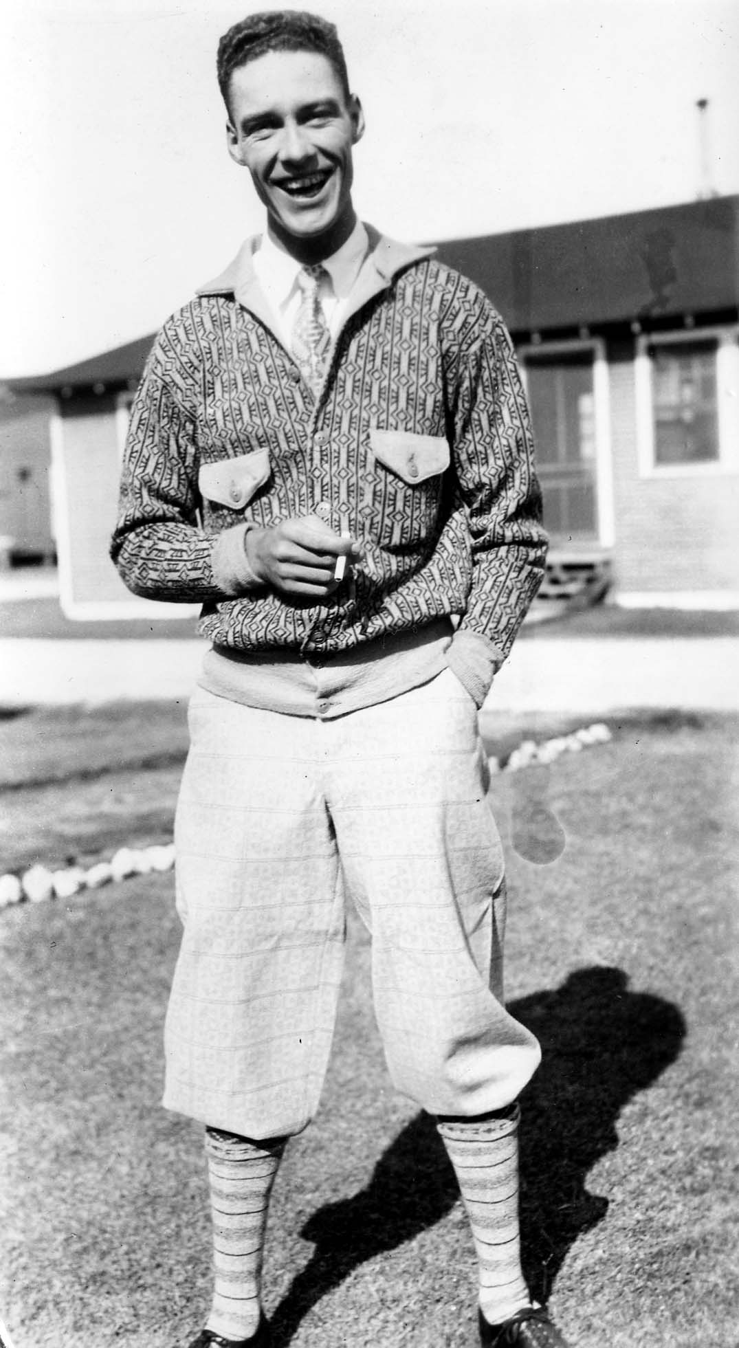 A smiling young Army aviator off-duty in 1920s knickerbockers, patterned knit sweater, and necktie holding a cigarette at Brooks Field.
