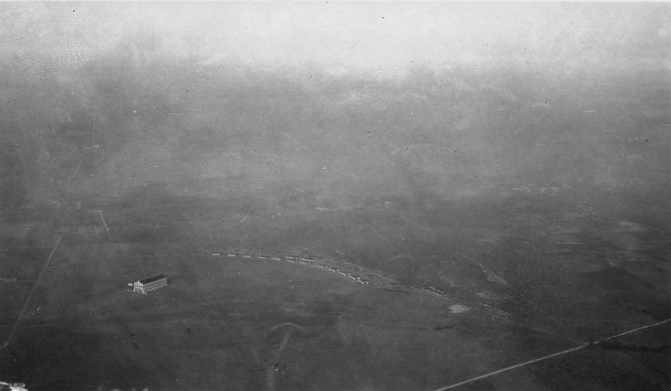 A hazy, high-altitude aerial photograph looking down at the scattered buildings and flat terrain of Brooks Field in Texas.