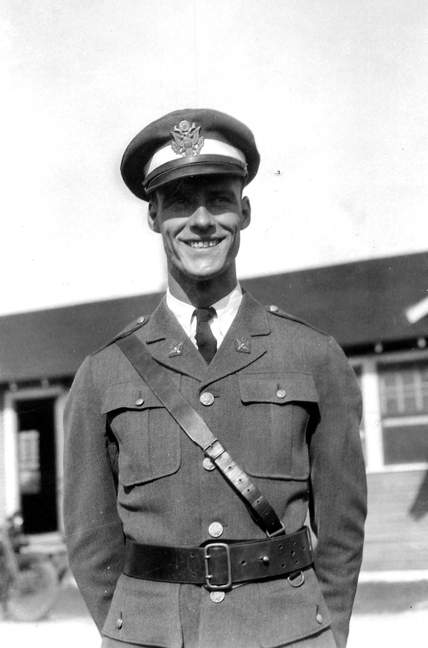 A portrait of a smiling military officer or cadet in a crisp dress uniform, service cap, and Sam Browne belt.