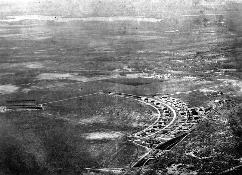 A sweeping aerial view of Brooks Field showcasing its iconic, semi-circular layout of aircraft hangars and support buildings.