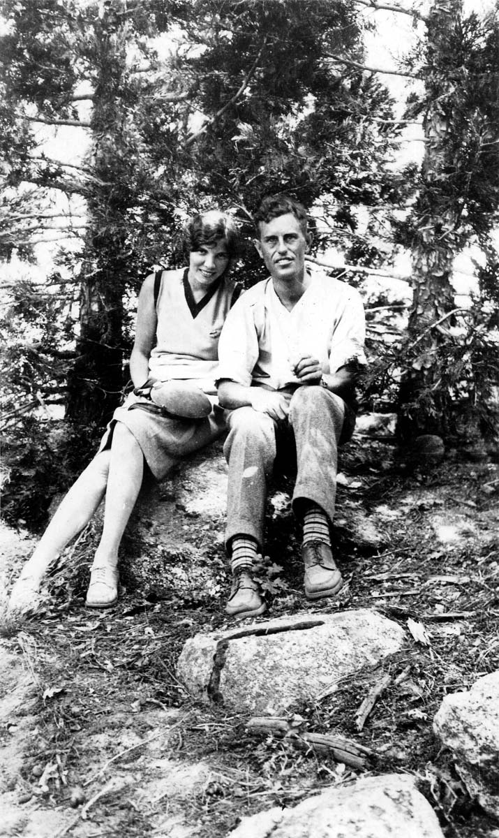 Donald A. Hall Sr. and a female companion sitting together on a rock beneath pine trees.