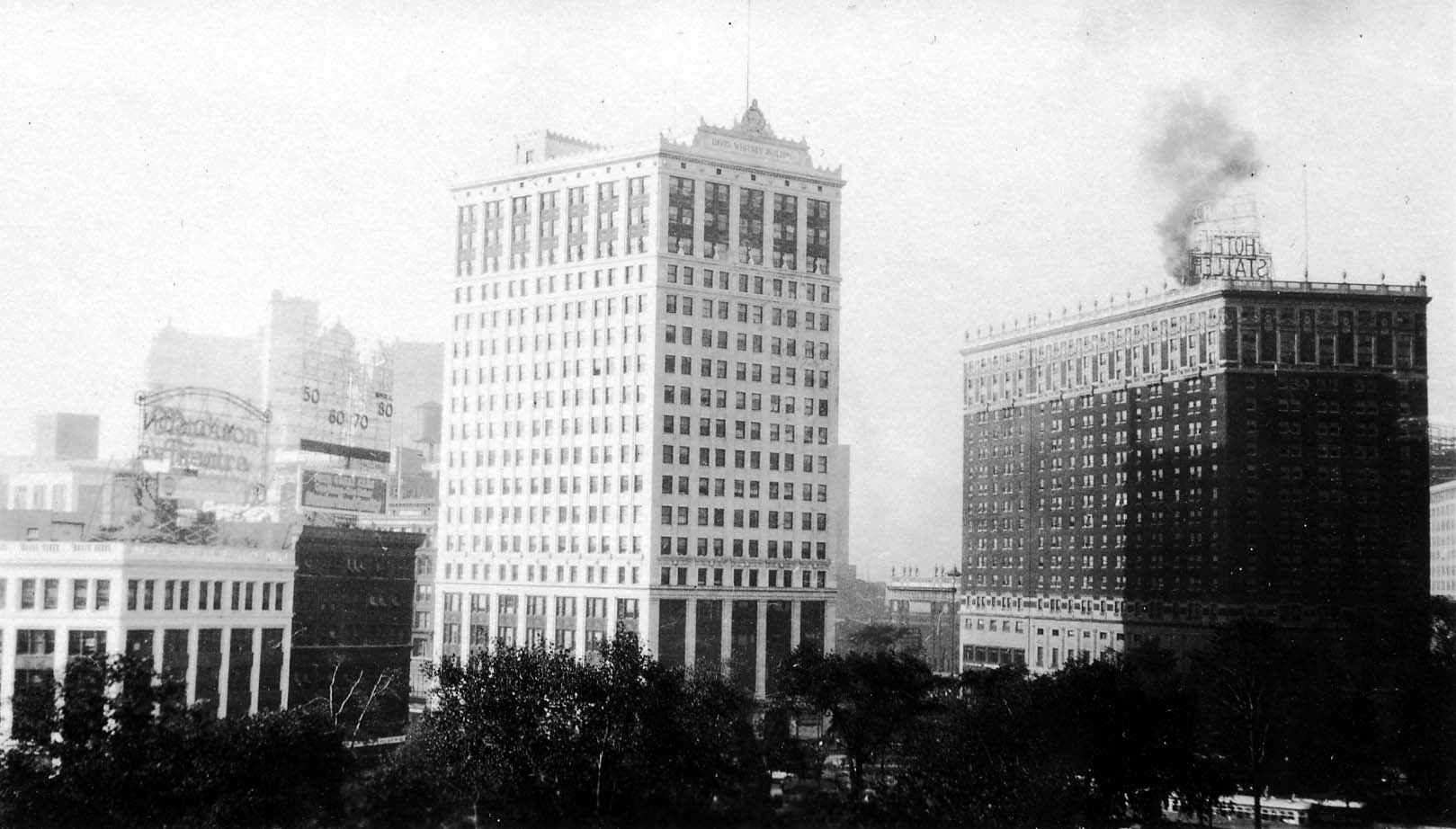 The towering white terra-cotta David Whitney Building and Hotel Statler overlooking the trees of Grand Circus Park in Detroit.