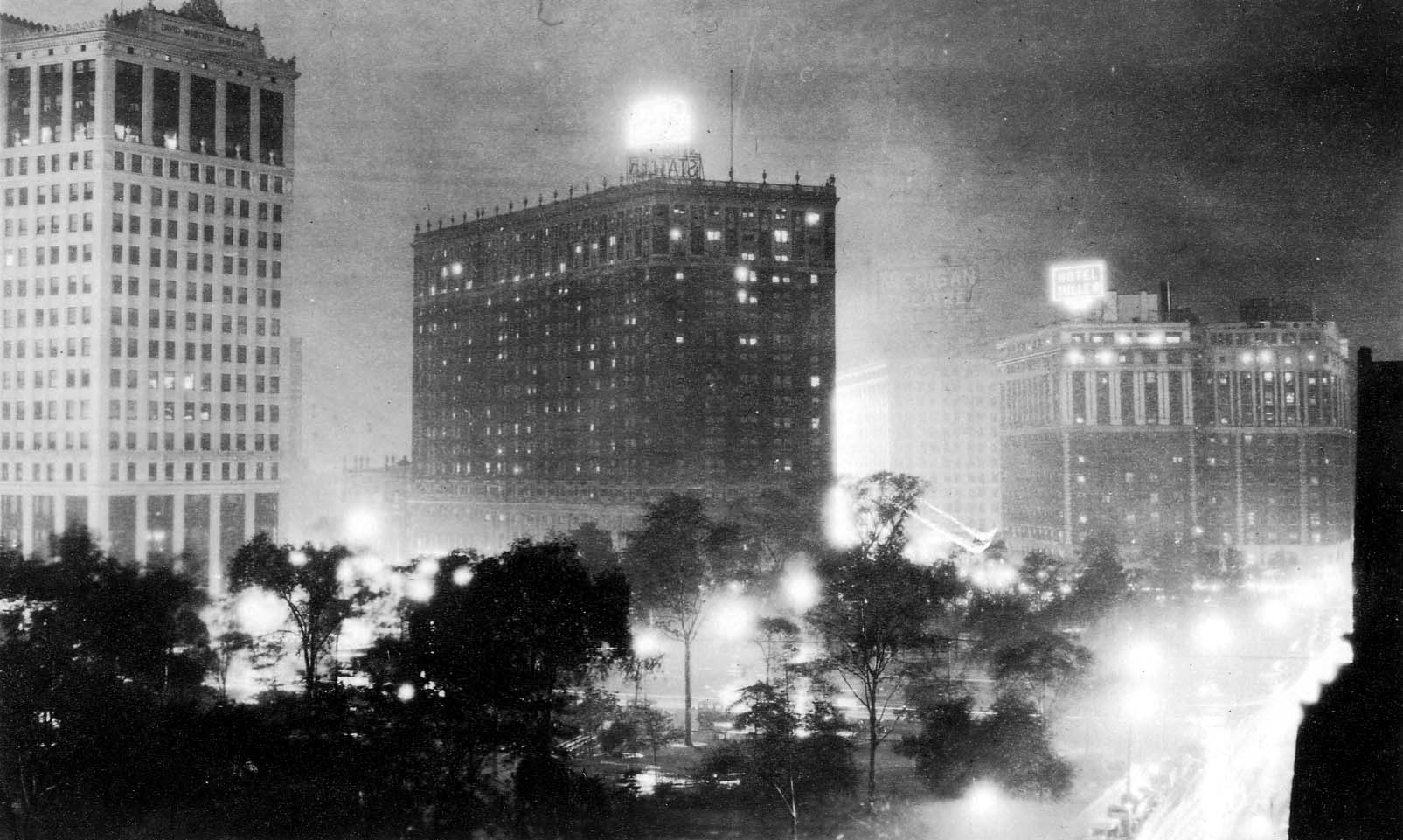 A panoramic night exposure of Grand Circus Park in Detroit, showcasing the illuminated Statler Hotel, the David Whitney Building, and glowing streetlamps.