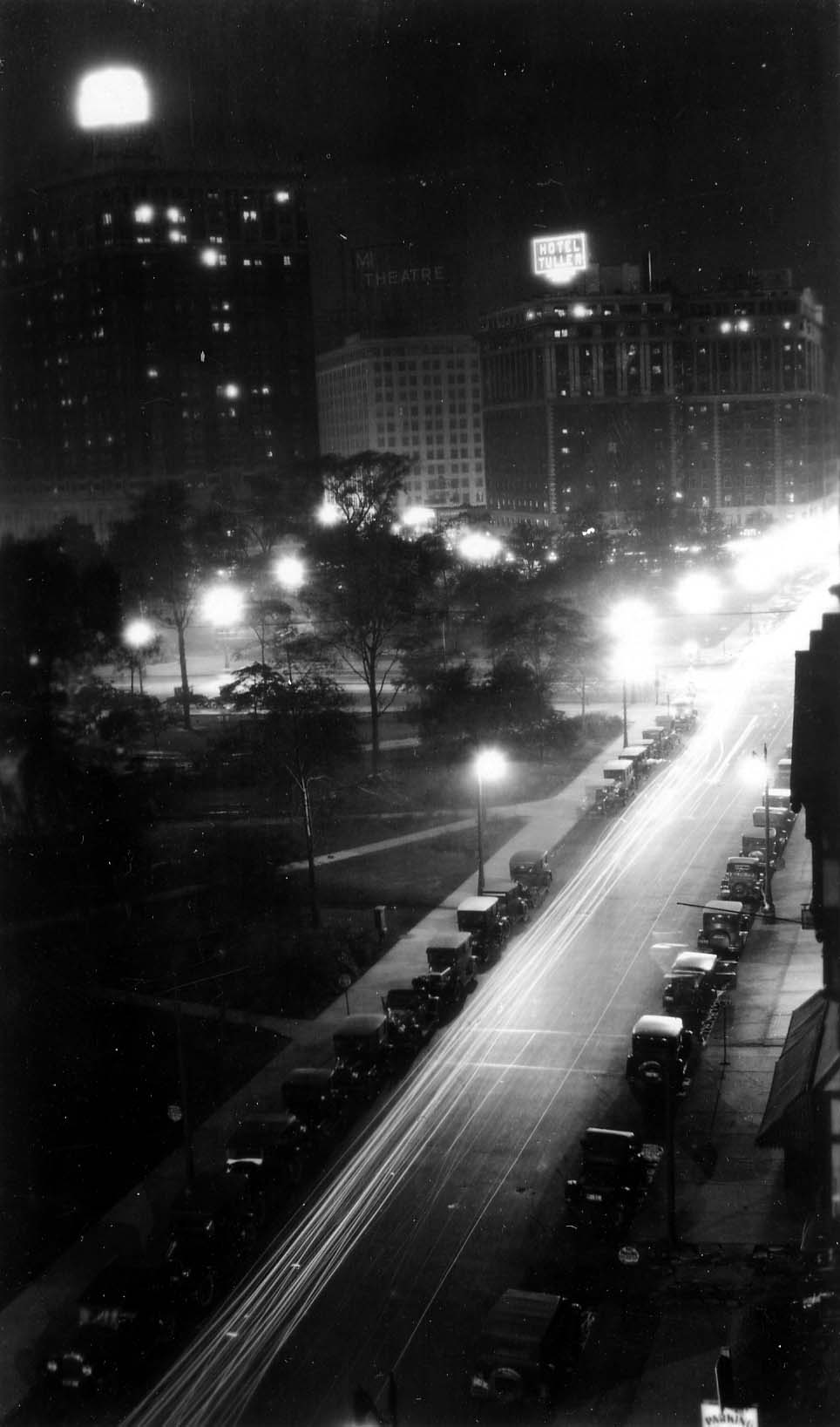 A vertical long exposure looking down the curve of Grand Circus Park toward the glowing rooftop signs of Hotel Statler and Hotel Tuller, with a 35-cent parking sign in the foreground.