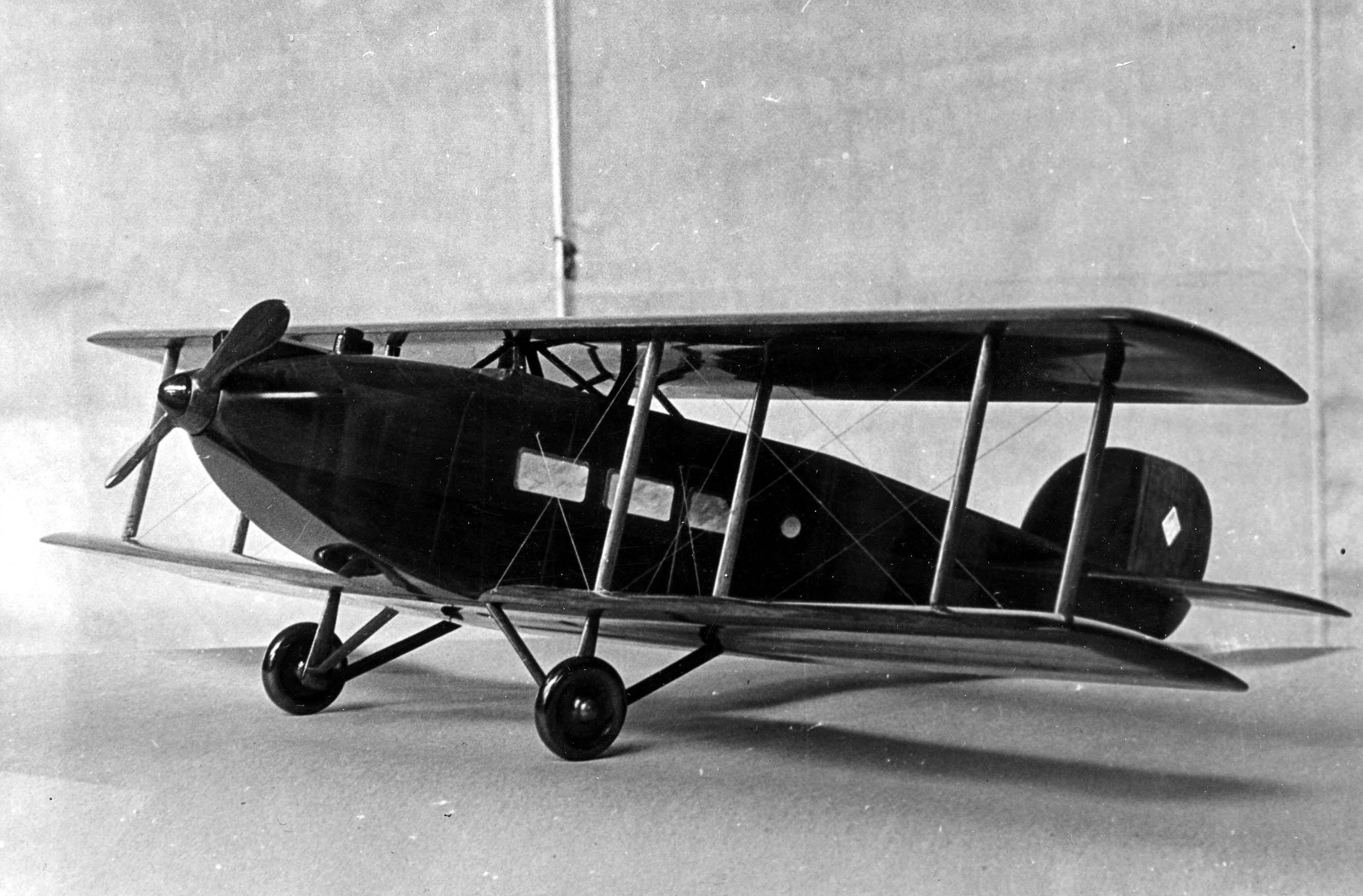 A carved and lacquered black wooden scale model of an early single-engine commercial cabin biplane transport with passenger windows.