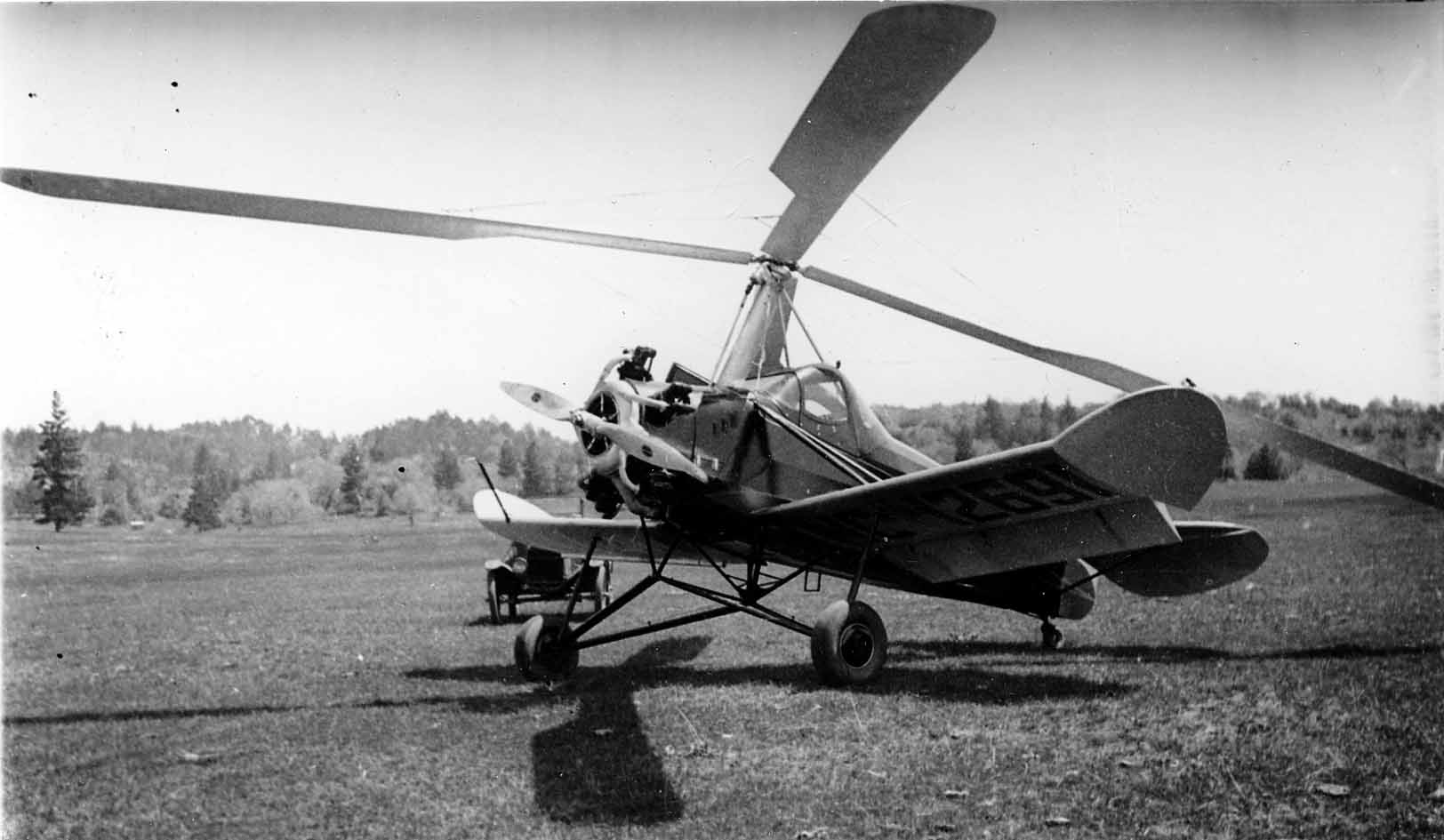 A parked experimental autogyro with a large radial engine, three-blade propeller, and a massive overhead rotor, sitting in a grassy field.