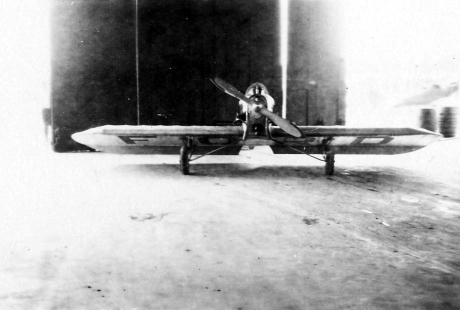 A small, single-seat, low-wing monoplane parked inside a hangar, with 'FORD' painted in massive letters across the underside of the wings.