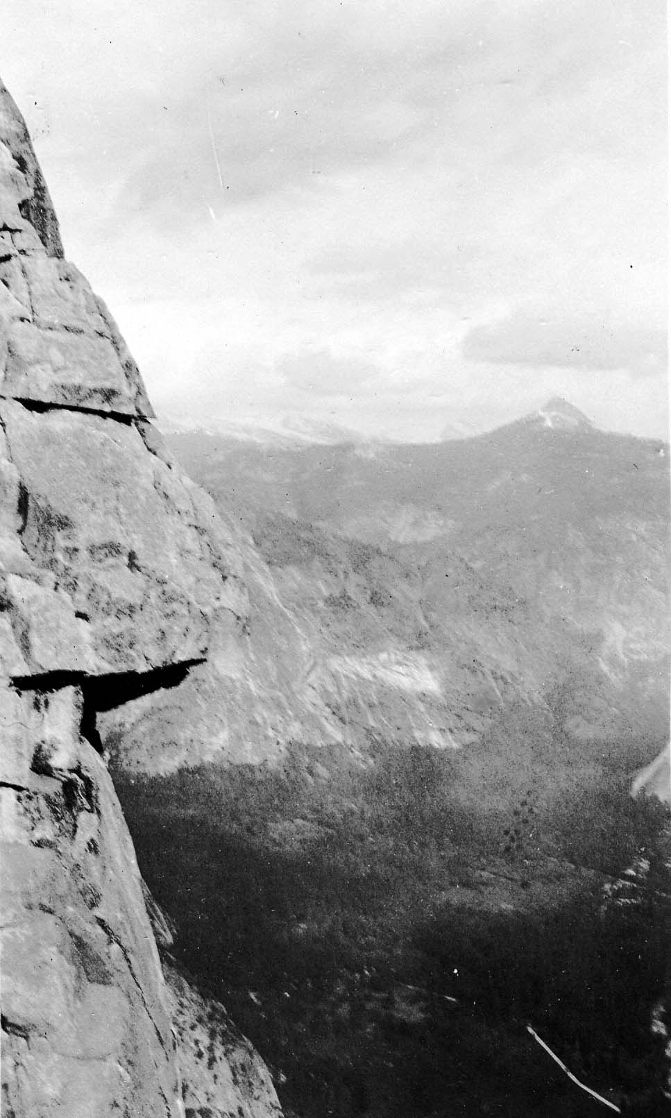 A dramatic vertical perspective looking past a sheer granite cliff edge down into the vast drop of Yosemite Valley.