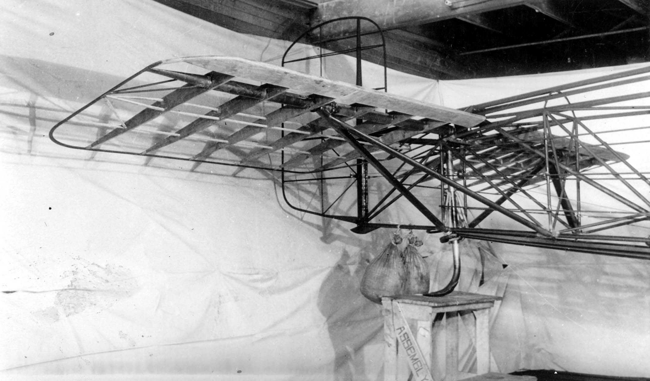 The uncovered tubular steel fuselage and wooden aft-wing framework of the experimental Hall X-1 on a test bench with a sandbag ballast.