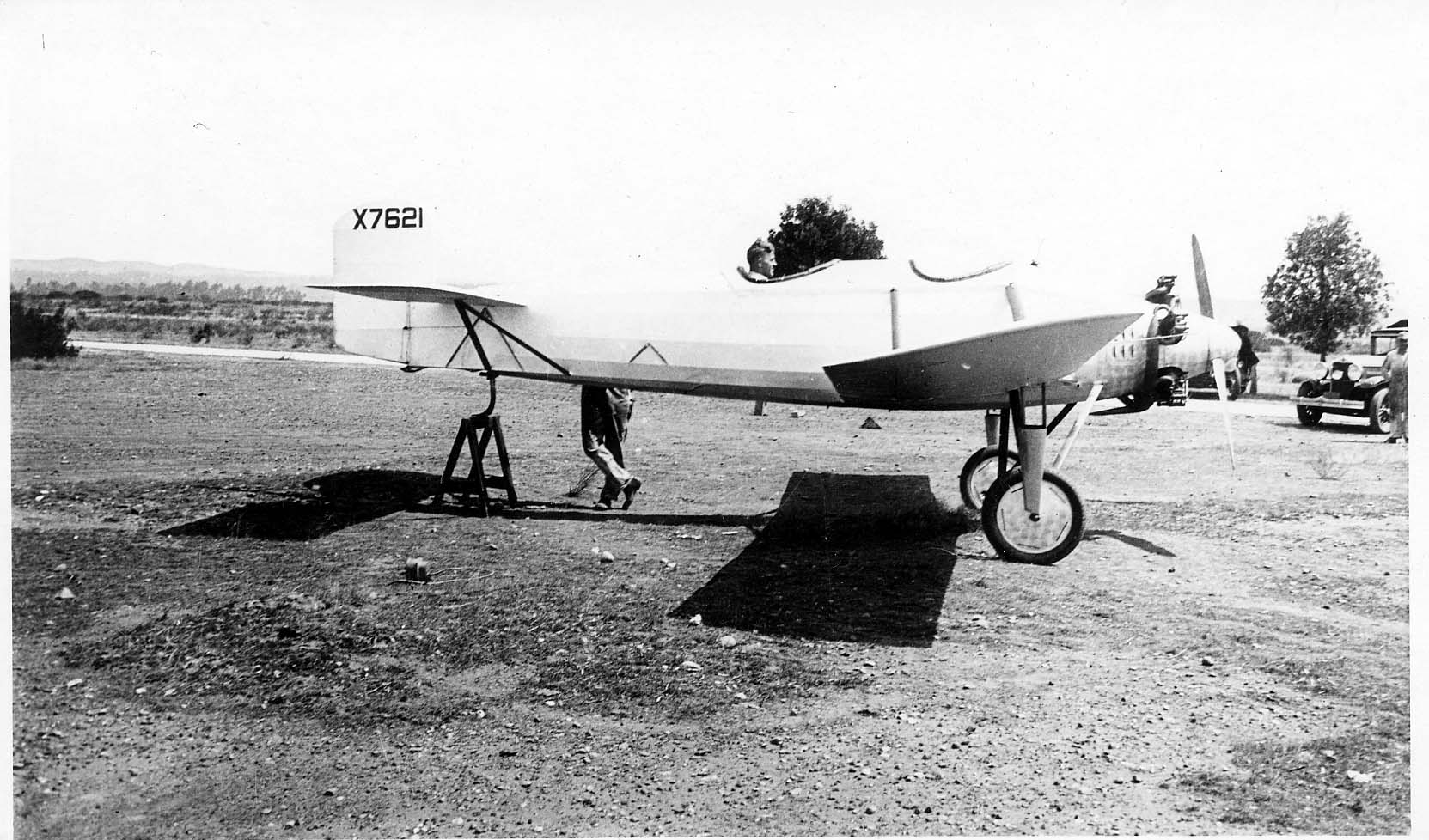 A side profile view of the Hall X-1 tandem-wing prototype on a dirt field with its tail supported on a sawhorse and pilot in the cockpit.
