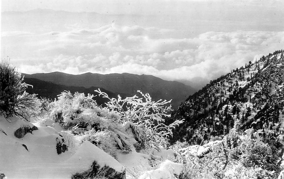 A breathtaking view from a high, snow-covered mountain ridge looking out over a vast sea of clouds filling the valley below.