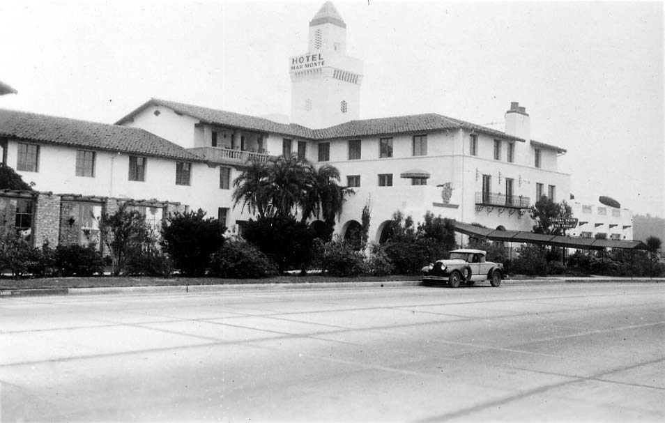 A wide exterior shot of the Hotel Mar Monte in Santa Barbara, showing the main entrance, dining room awning, and a vintage car parked out front.