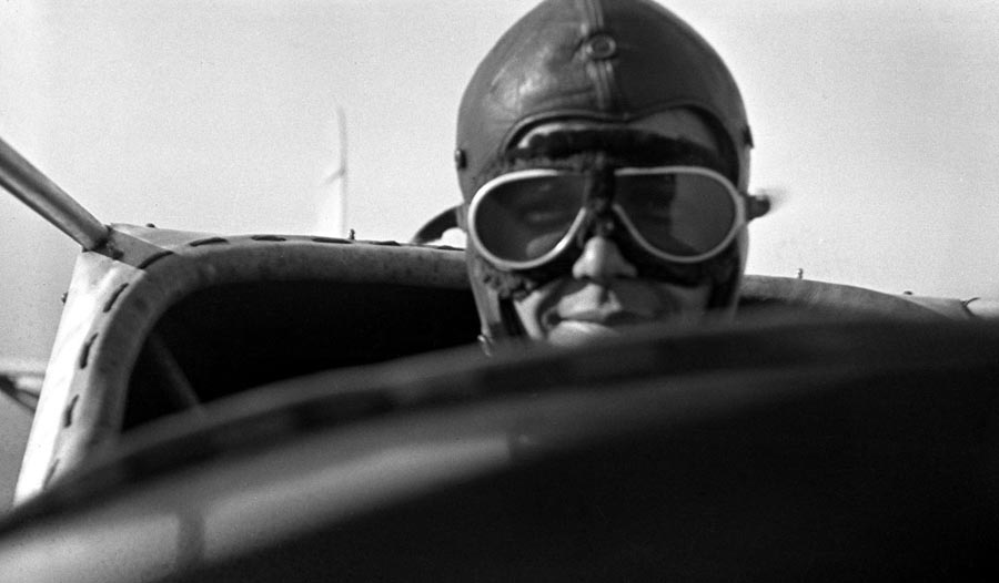 Charles Lindbergh wearing a leather flying helmet and goggles, sitting in the open cockpit of a Ryan M-1 high-wing monoplane.