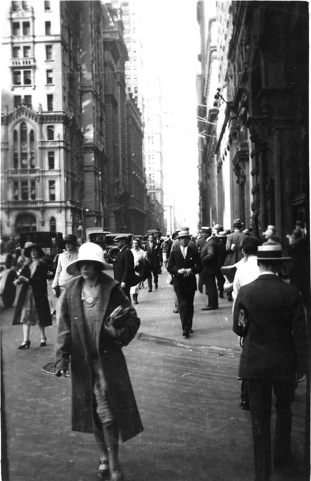 A bustling street-level view looking down a narrow Lower Manhattan canyon filled with pedestrians in 1920s cloche hats and straw boaters during the Lindbergh celebrations.