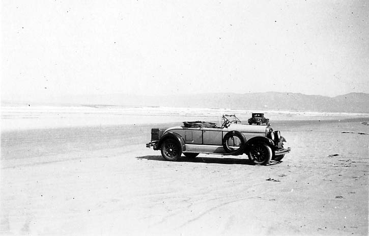 Donald A. Hall Sr.'s personal yellow 1925 Studebaker Roadster with a folded soft top and side-mounted spare tire parked on the wide sand of a California beach.