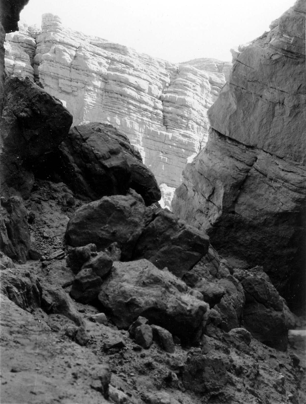 A tight framing of a narrow rocky canyon passage, with bright sunlight illuminating the textured cliff faces and jumbled boulders.