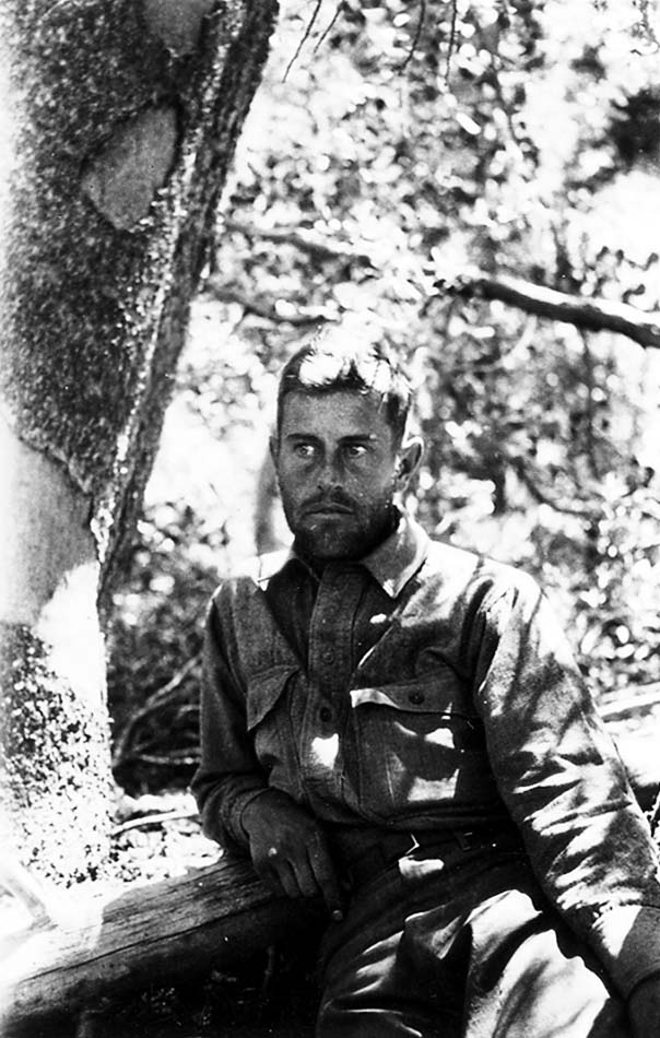 A bearded Donald A. Hall Sr. resting in dappled shade against the trunk of a tree.