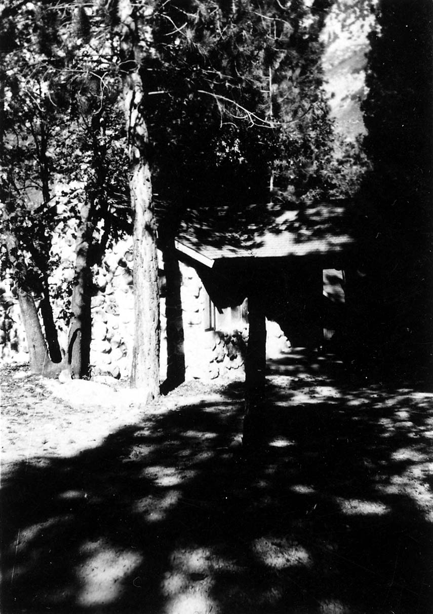 A rustic stone and timber mountain cabin nestled in dappled shade among tall pine trees in the San Bernardino Mountains.