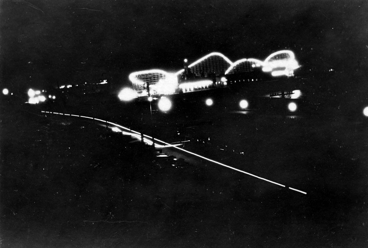 A night long-exposure photograph showing the illuminated outlines and undulating tracks of the wooden roller coaster on the Santa Monica Pier.