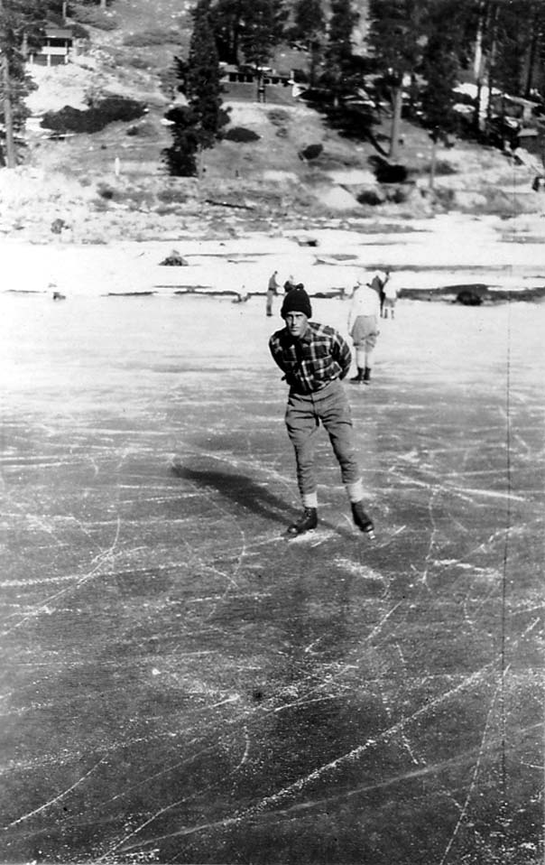 A self-portrait of Donald A. Hall Sr. wearing a plaid jacket and a knit cap, gliding toward the camera on a frozen lake with his hands clasped behind his back.