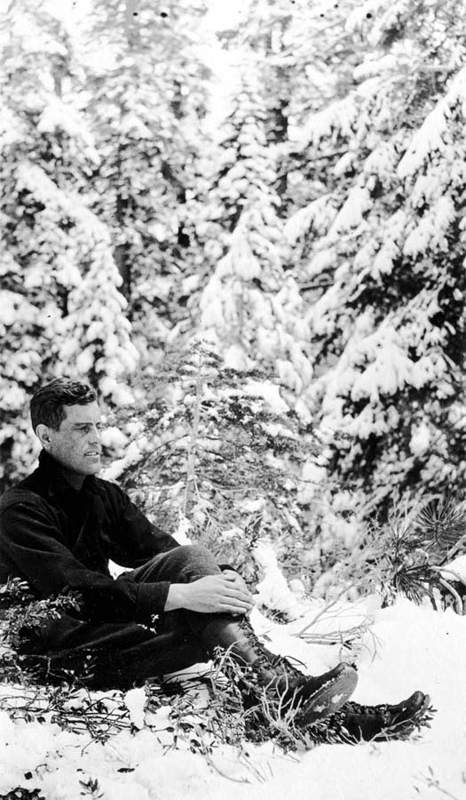 A contemplative self-portrait of Donald A. Hall Sr. sitting thoughtfully in deep snow, surrounded by pine trees.