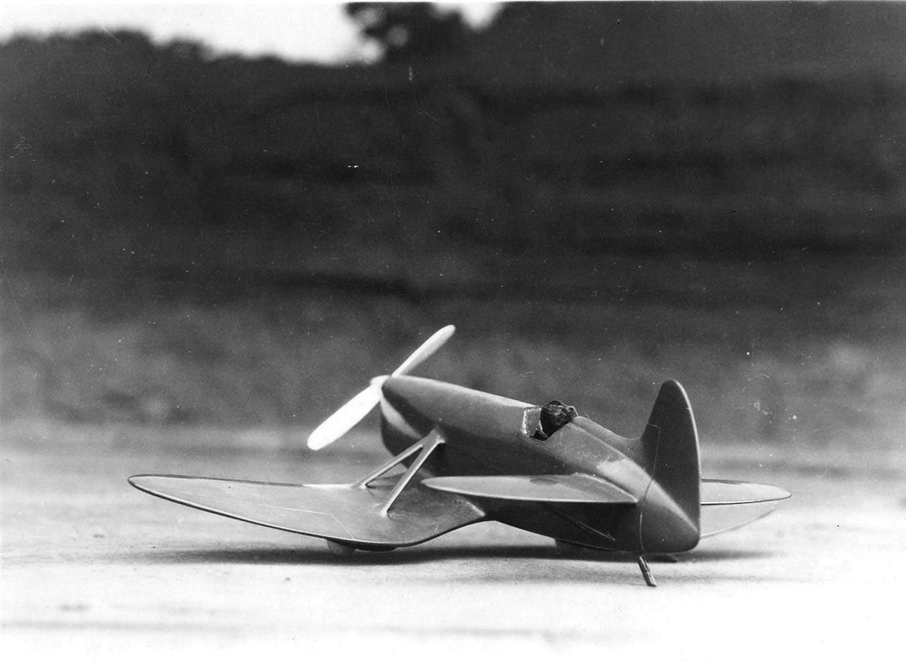 A dark, sleek wooden wind tunnel model of a single-engine aircraft resting on a textured roof surface.