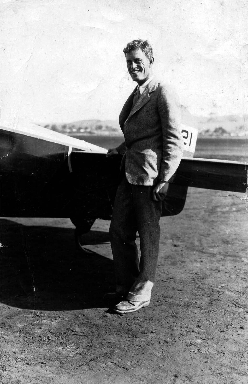 Donald A. Hall standing by the tail of an aircraft on an unpaved airfield smiling at Dutch Flats.