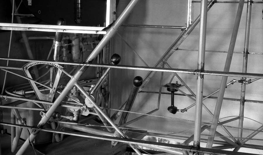 The raw, uncovered tubular steel framework of the Spirit of St. Louis cockpit, showing the control stick, rudder pedals, and the side window frame.