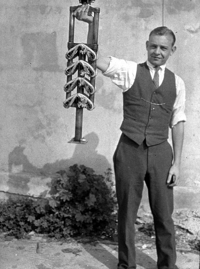 An unidentified factory worker proudly holding up a completed, heavy-duty bungee cord shock absorber assembly for the landing gear.