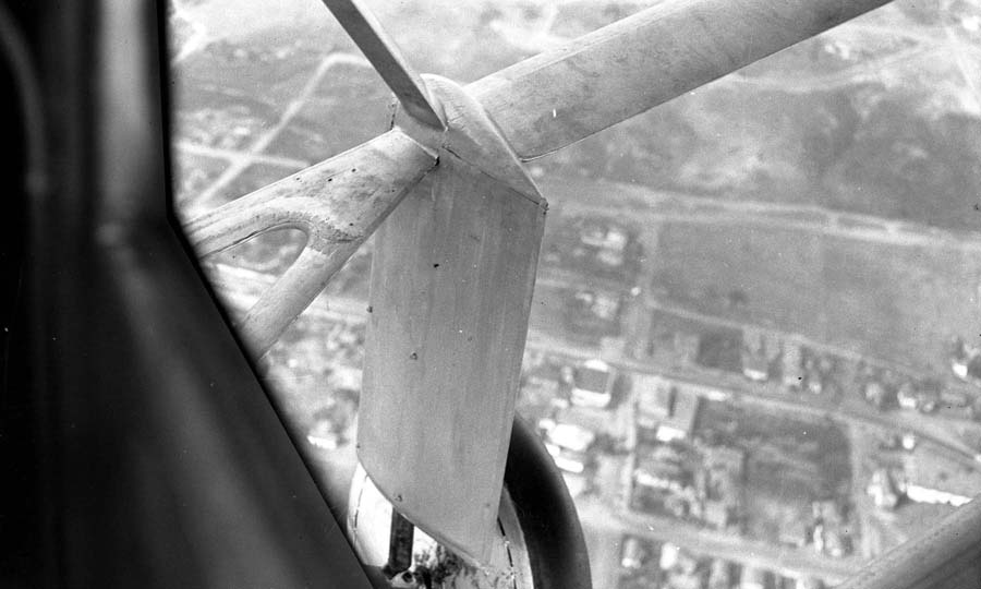 A first-person perspective looking out the side window of the Spirit of St. Louis at the wing struts and the city of San Diego far below.
