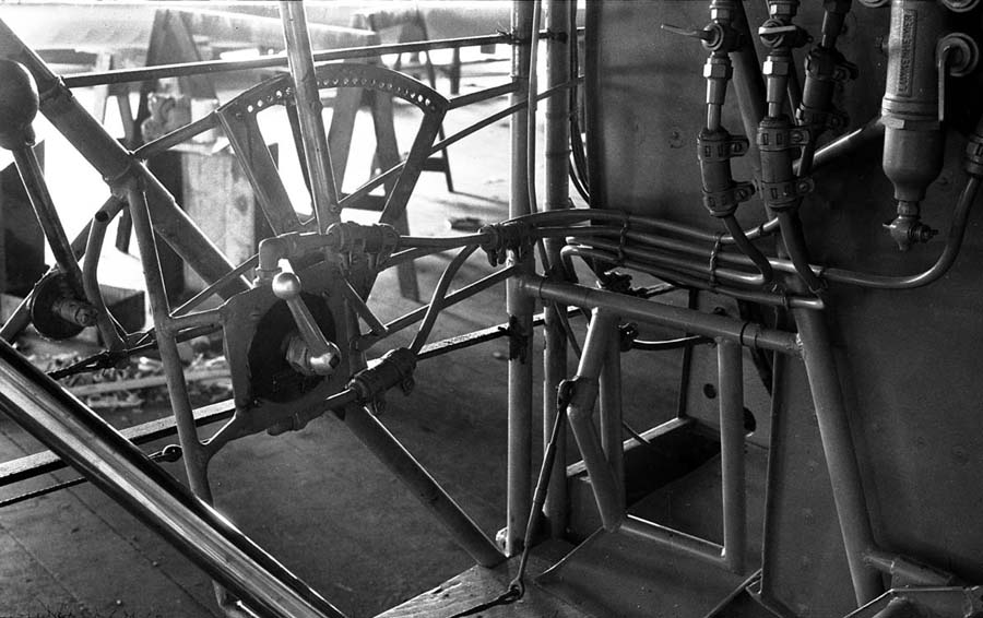 A close-up view inside the raw tubular steel cockpit of the Spirit of St. Louis, focusing on the mechanical flight controls and fuel routing.