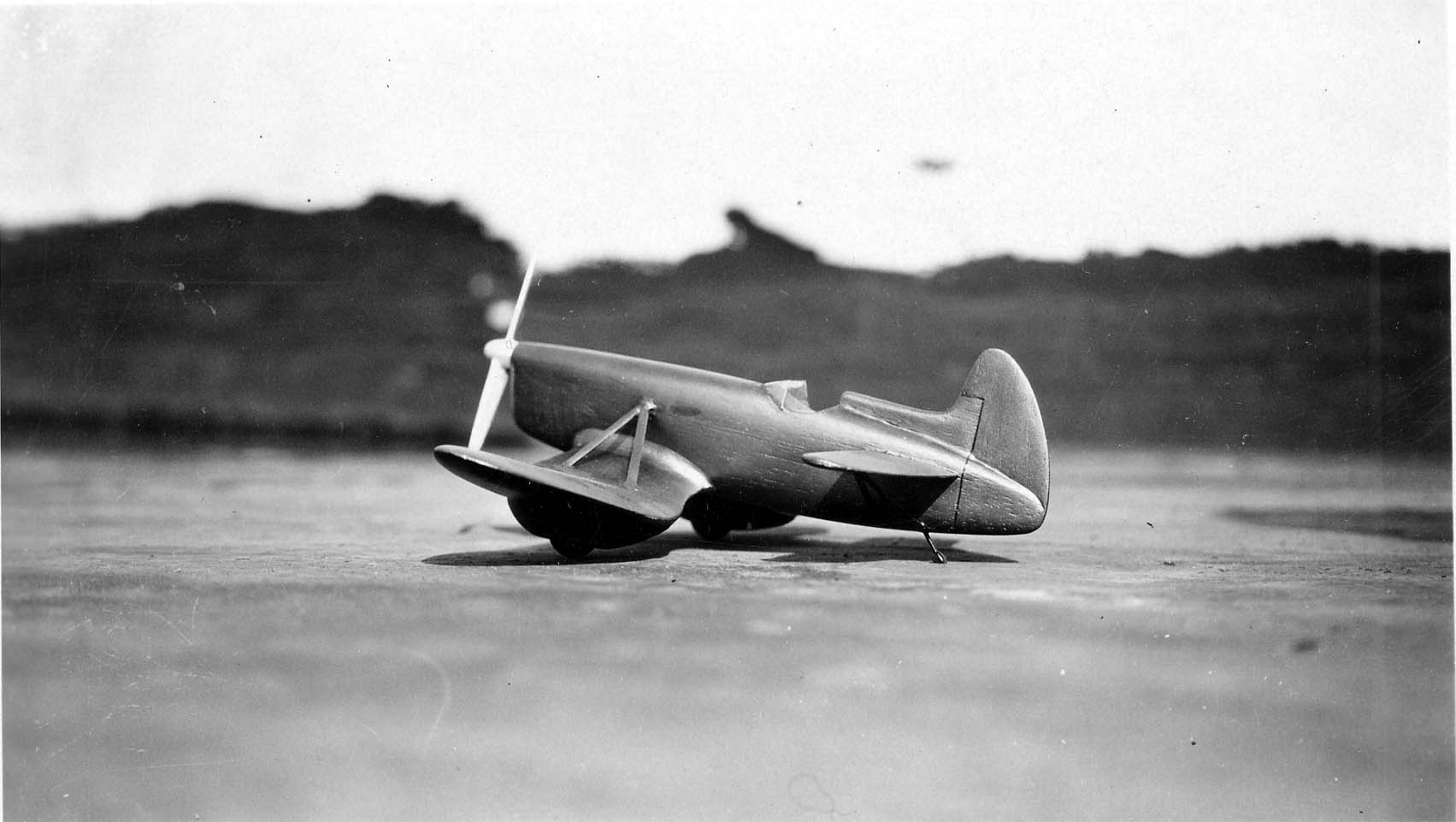 A side profile of a wooden tandem wing aircraft model with a forward and rear wing, resting on a rooftop.