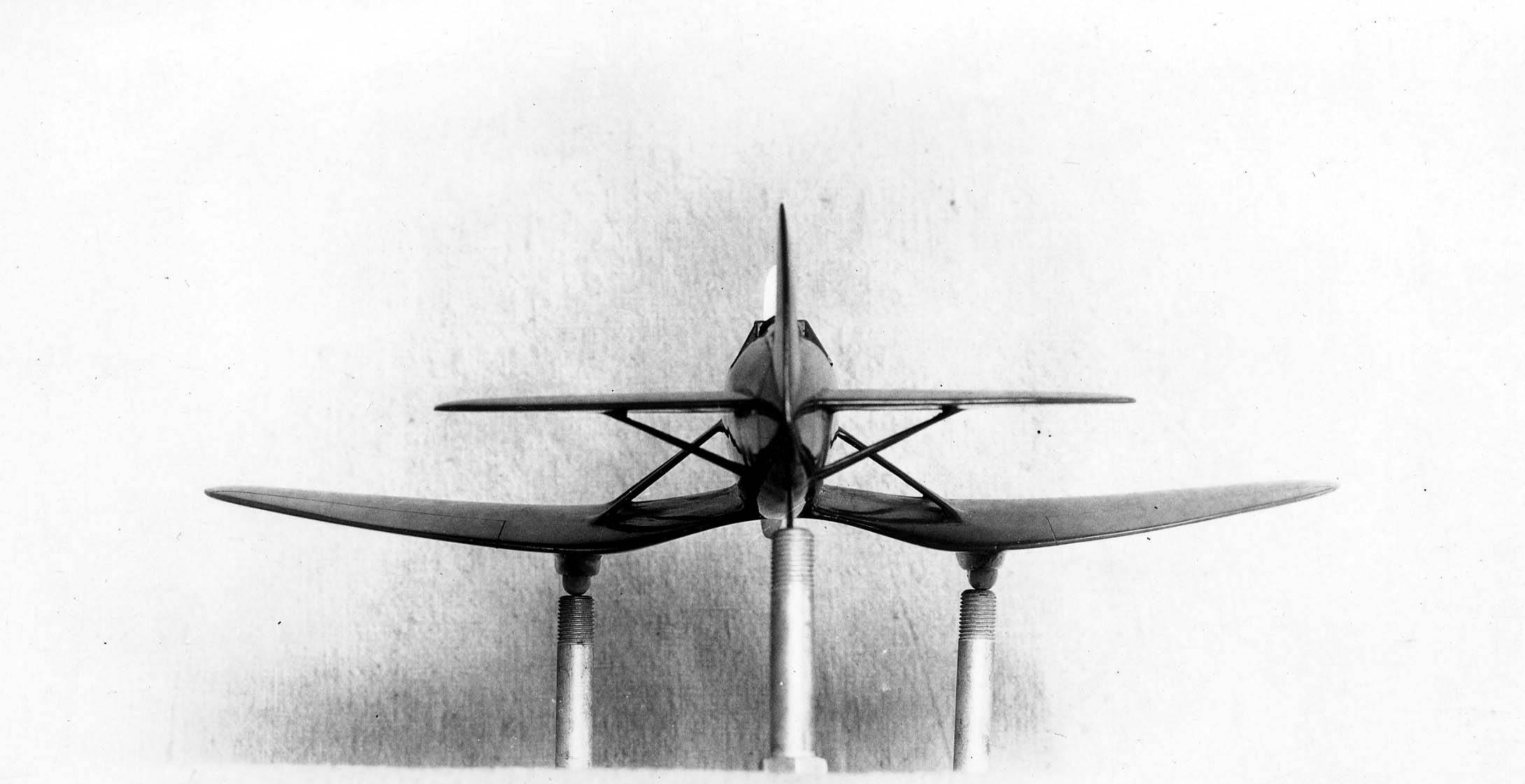 A rear view of a dark tandem wing aircraft model mounted on three metal pegs for wind tunnel testing.