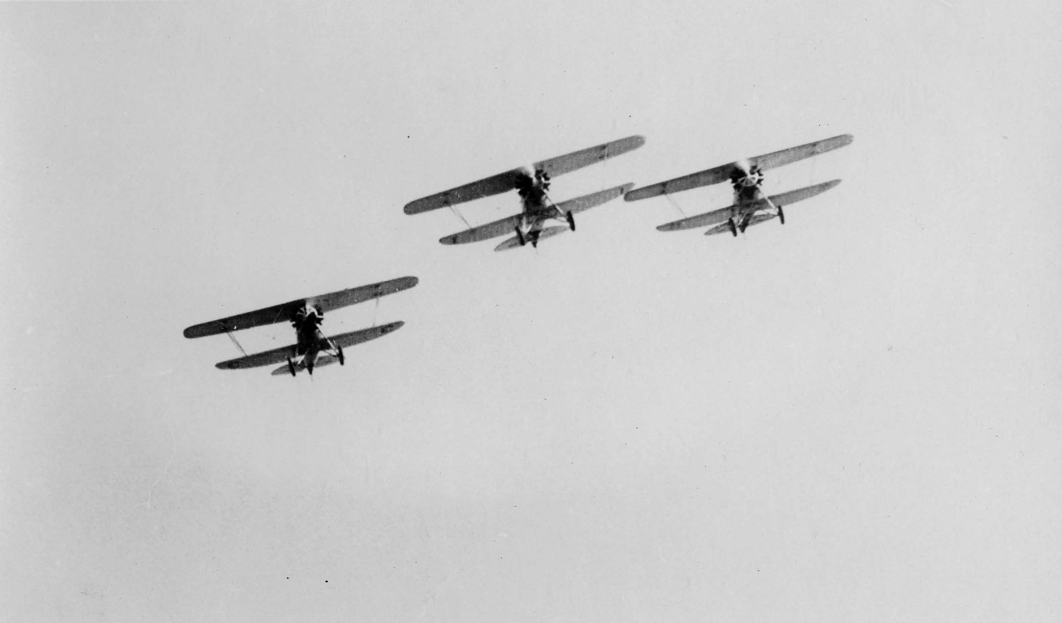 Three biplanes executing a sharp, coordinated banking turn in a tight V-formation.