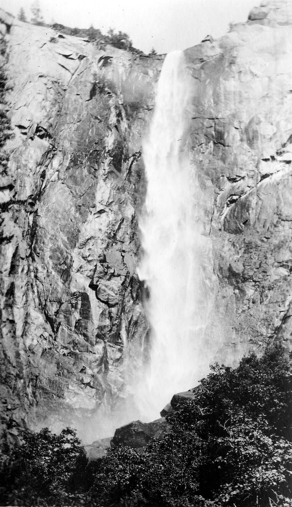 A direct vertical view of Upper Yosemite Fall roaring down a sheer fractured granite cliff into a billowing cloud of spray.