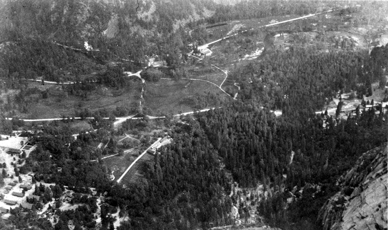 A dizzying high-elevation overlook looking down from the granite rim onto the roads, meadows, and pine forests of the Yosemite Valley floor.