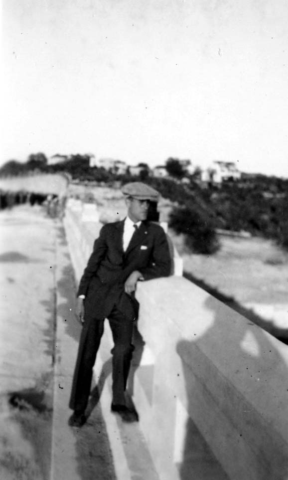 Young Donald A. Hall in a suit and flat tweed cap leaning against a concrete bridge balustrade in San Diego.