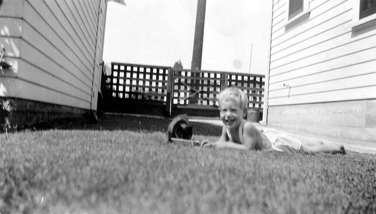 A young toddler, Don Hall Jr., lying in the grass in a bright yard, smiling directly at the camera.