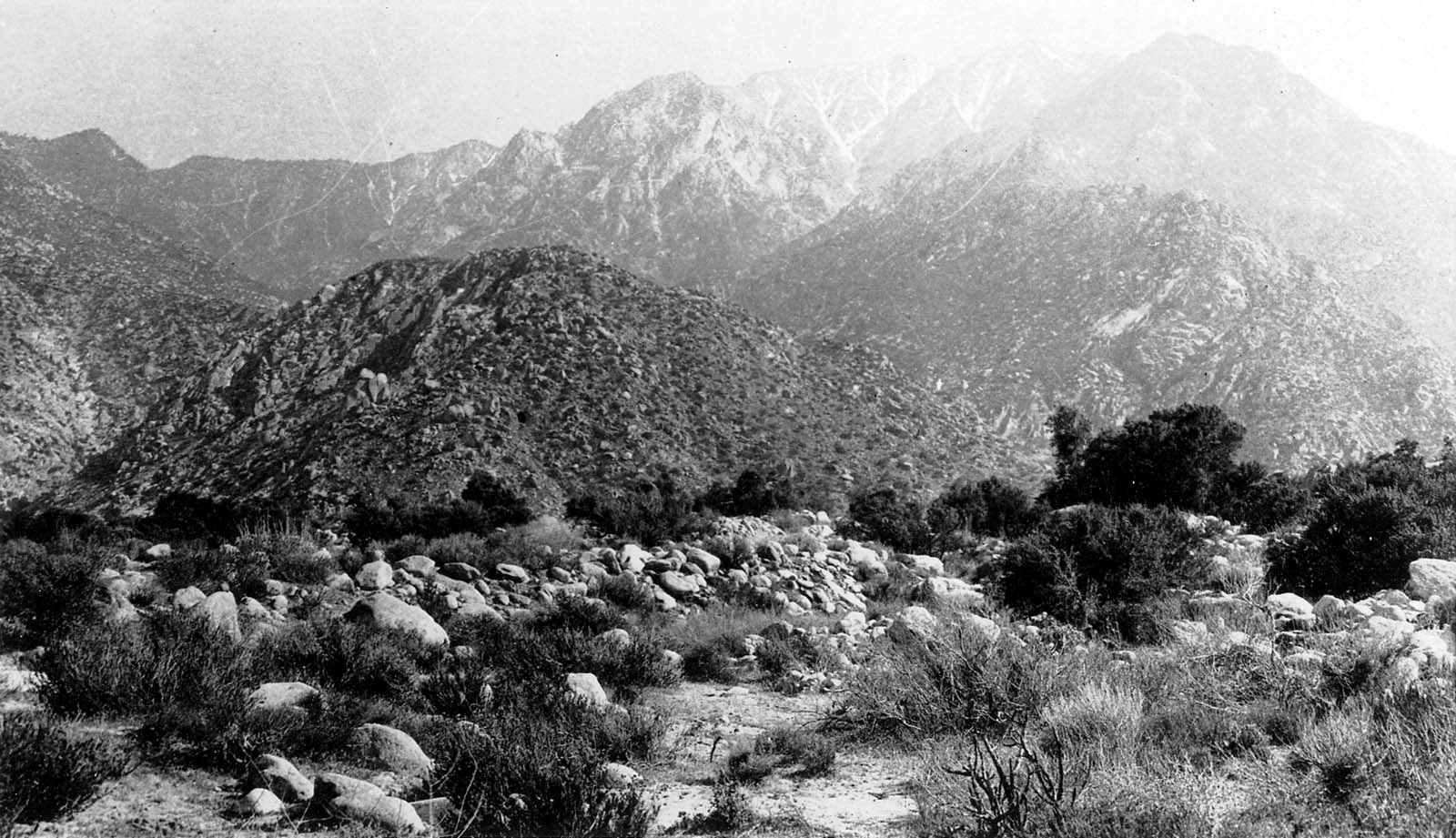 An expansive view of rolling mountain foothills covered in sparse desert brush under a bright, hazy sky.