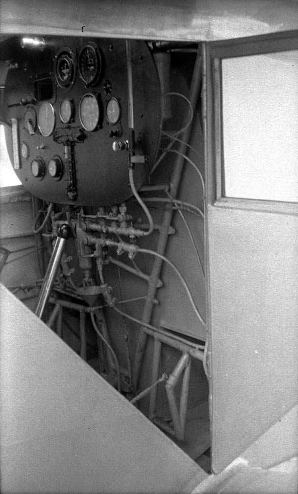 Interior view through the open cockpit door showing the instrument board and complex lower fuel plumbing manifold.