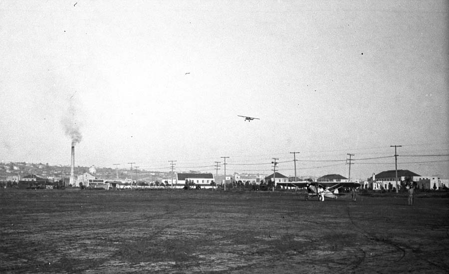 Airfield overview showing parked aircraft on flightline and the Spirit of St. Louis flying high overhead.