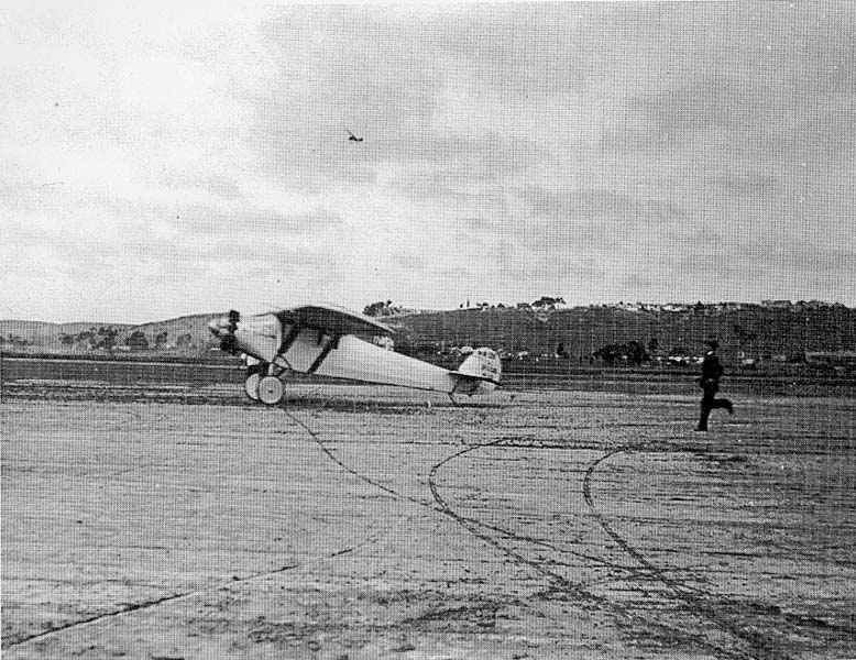 Airfield photograph of the Spirit of St. Louis landing rollout at Dutch Flats with a man running across the dirt field.
