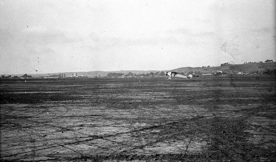 Long-distance airfield photograph of the Spirit of St. Louis rolling out across Dutch Flats at touchdown.