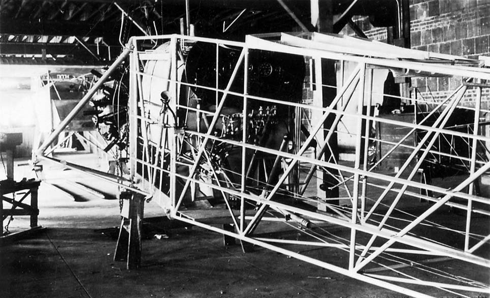 Factory view of uncovered steel-tube fuselage truss on sawhorses with Wright Whirlwind engine mounted.